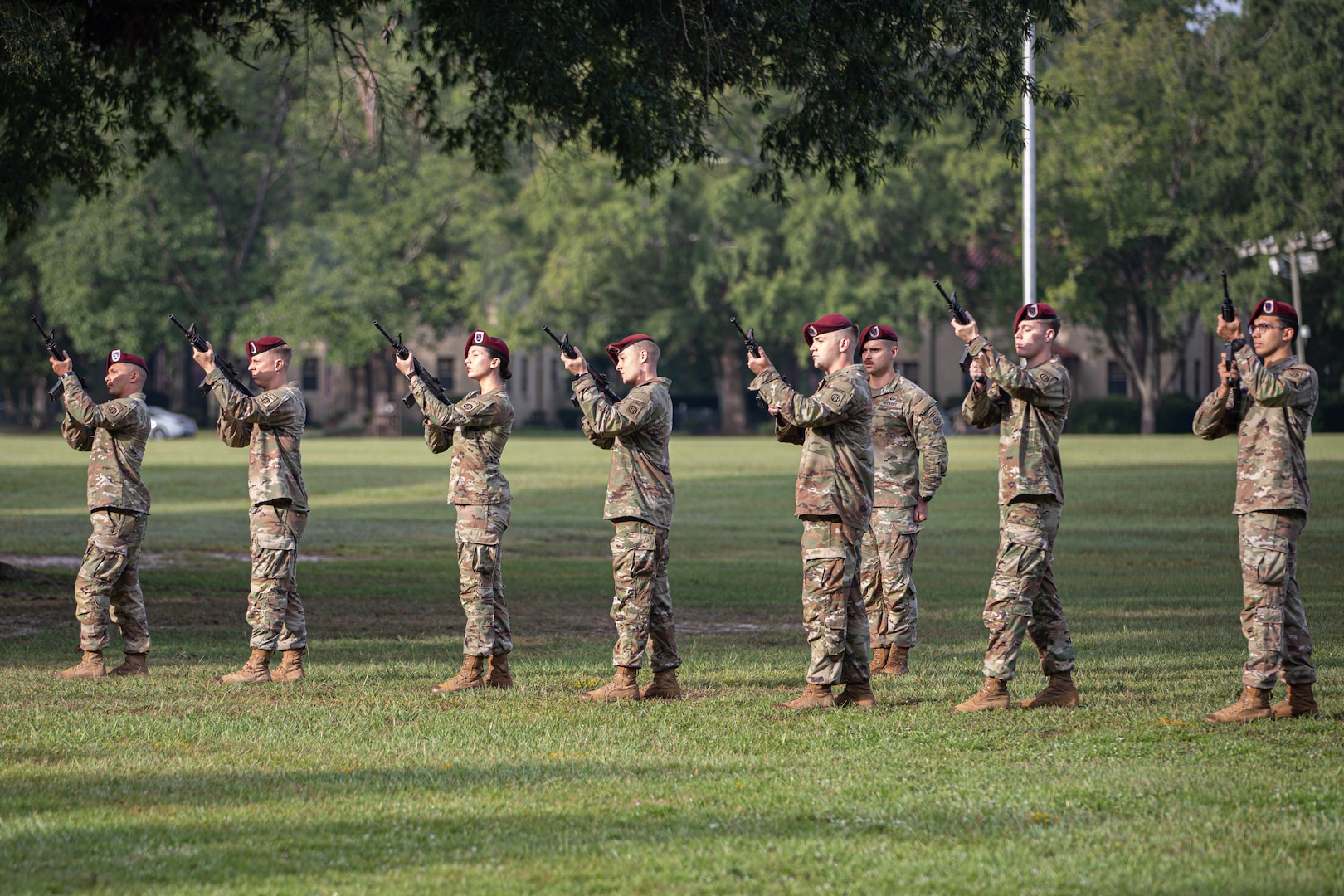 Soldiers in camouflage military uniforms with red berets point rifles in the air.