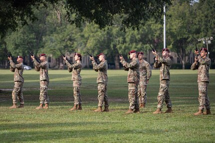 Soldiers in camouflage military uniforms with red berets point rifles in the air.
