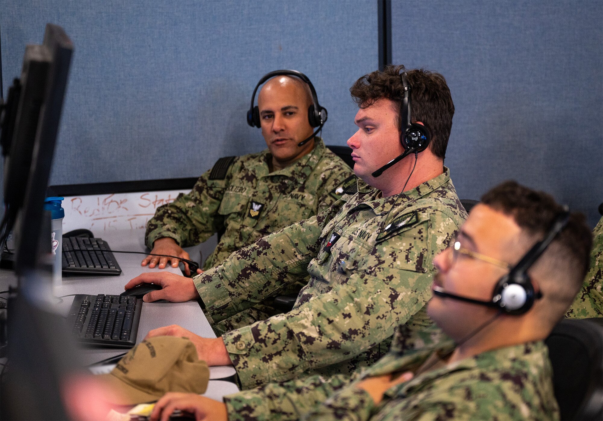 uniformed U.S. Sailors wearing headsets work at computers