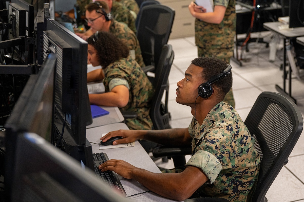 uniformed U.S. Marines wearing headsets work at computers