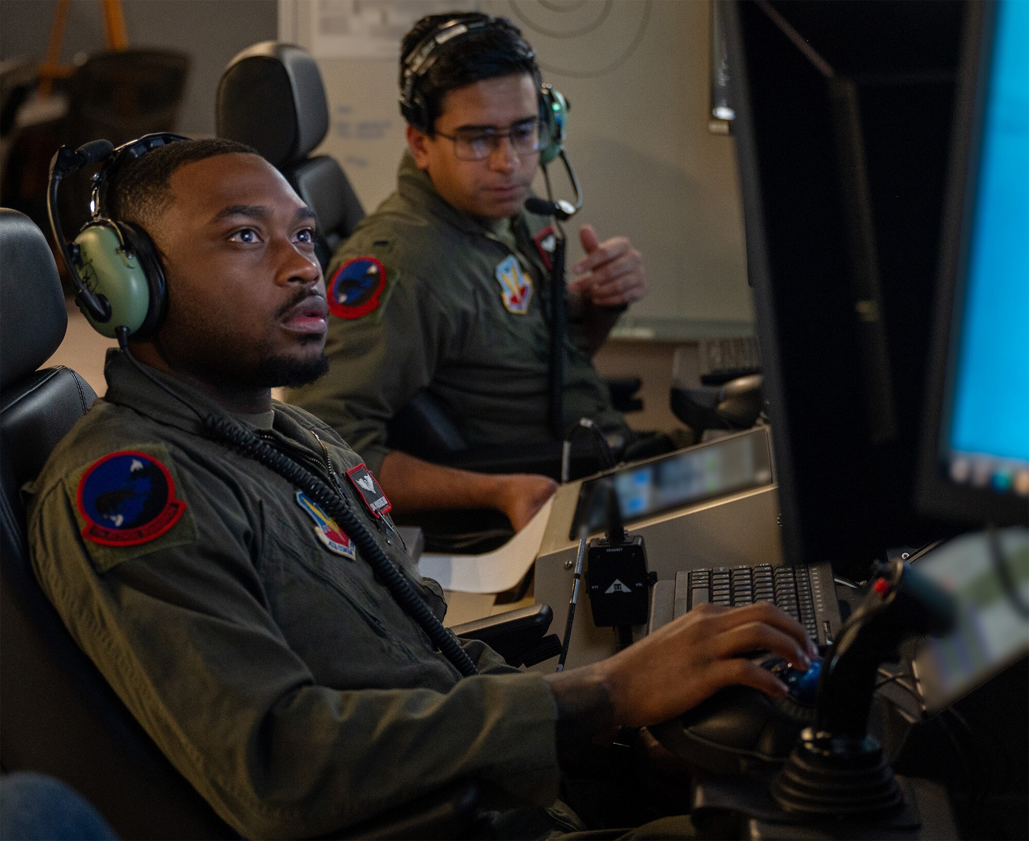 uniformed U.S. Airmen wearing headsets fly MQ-9 simulators