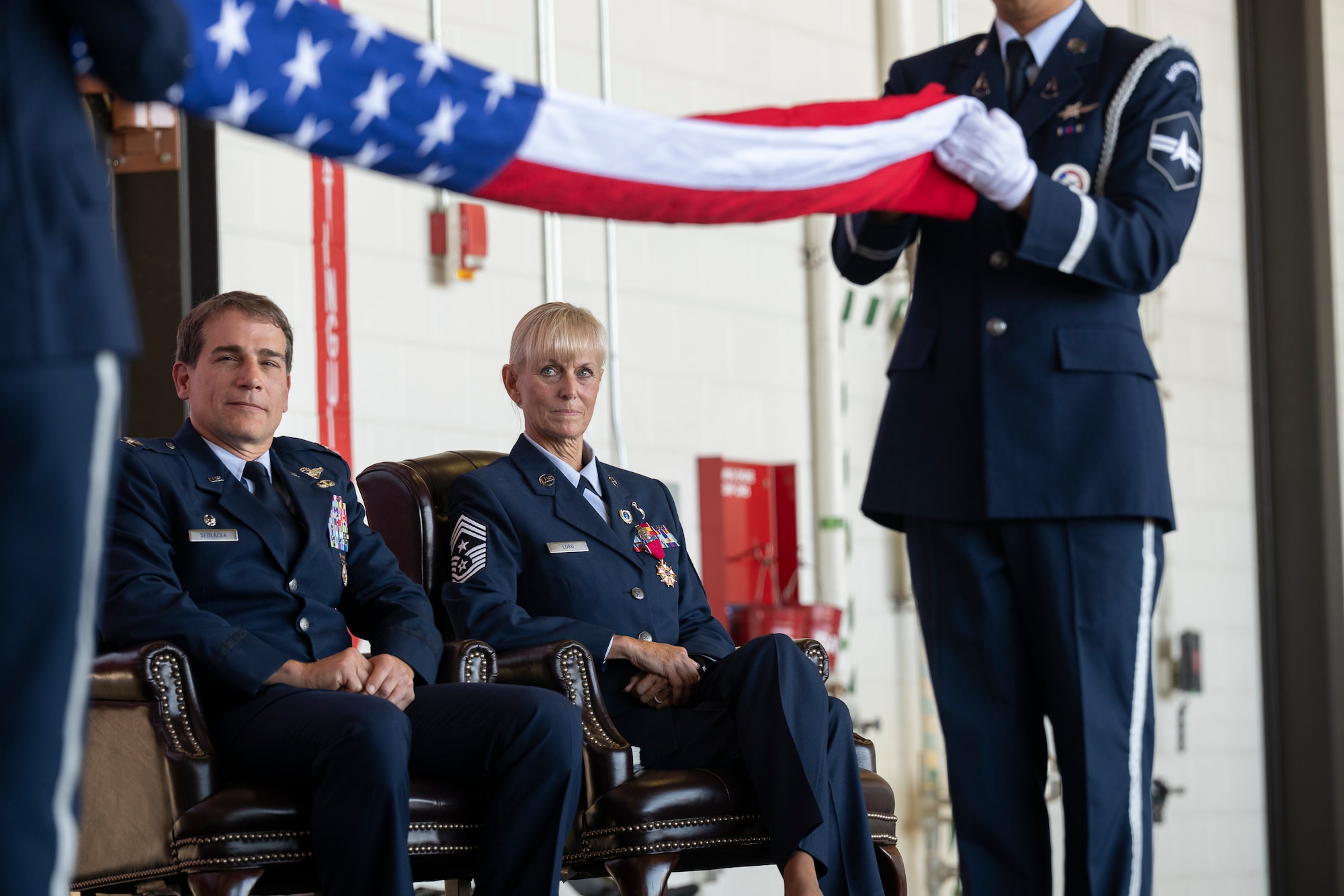 Two military servicemembers watch two others fold an American flag.