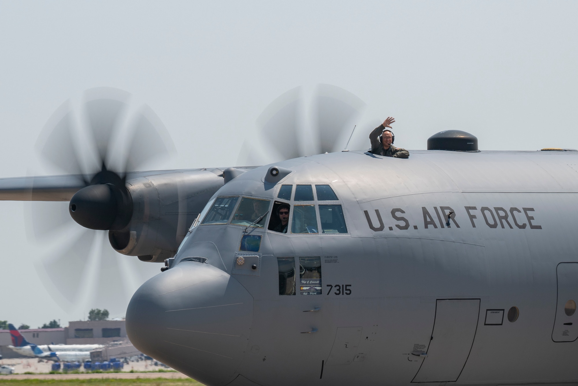 A man waves from a hole atop a military aircraft.