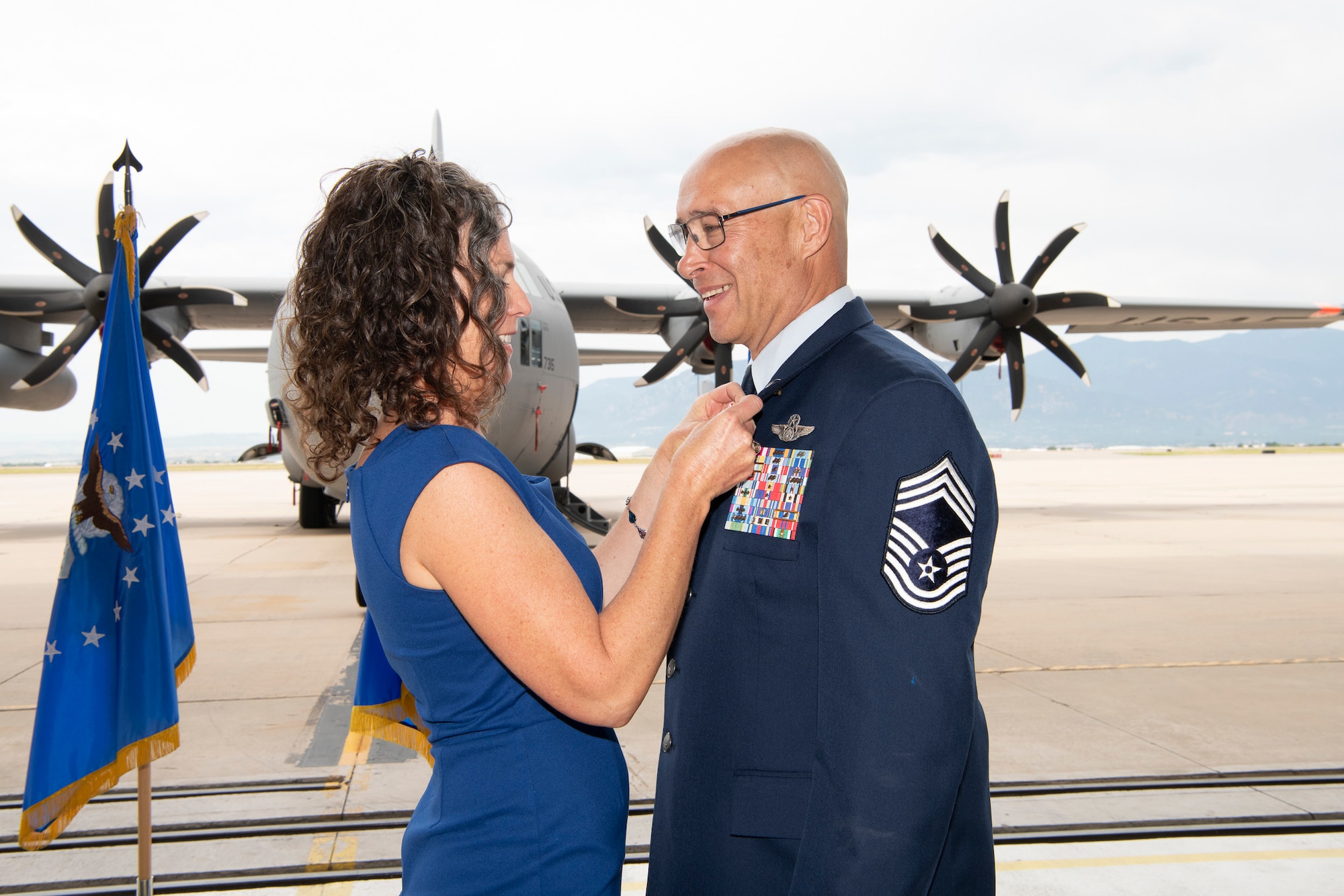 A civilian woman secures a pin to the uniform of a man wearing military service dress.