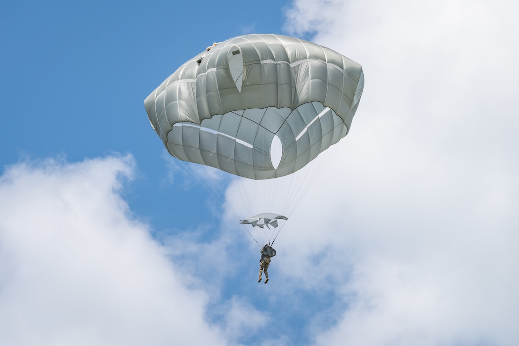 A lone parachute jumper can be seen over white clouds and deep blue sky