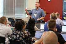 A man standing with an animated engagement delivery provides attendees with information during  the PROMIS rollout.