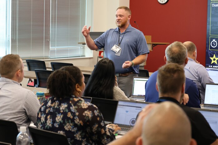 A man standing with an animated engagement delivery provides attendees with information during  the PROMIS rollout.