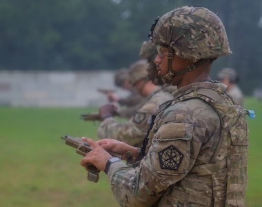 A row of Army soldiers in combat uniforms with helmets are adjusting their pistols at a firing range.
