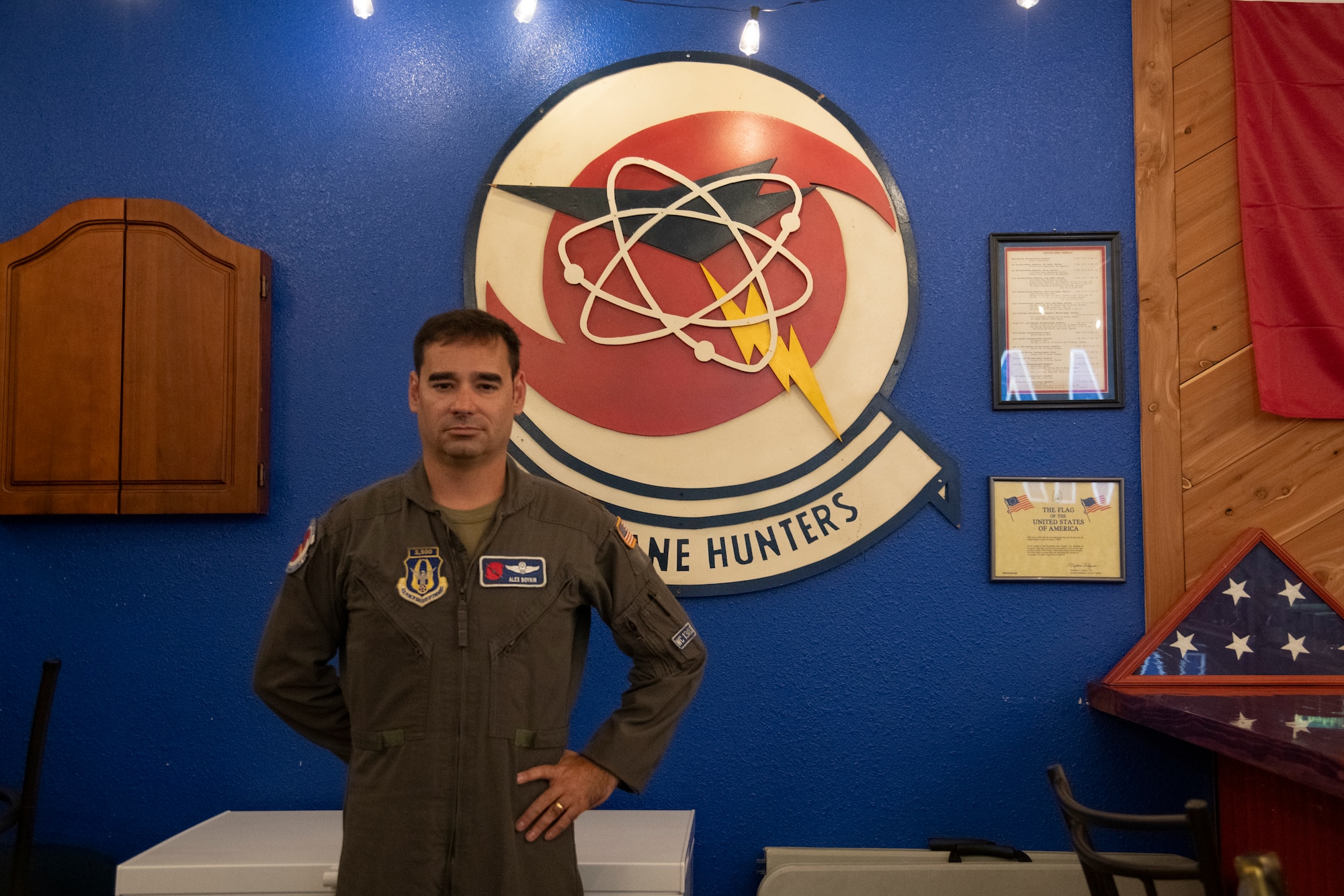 Maj. Alex Boykin stands in front of a sign of the Hurricane Hunters patch.