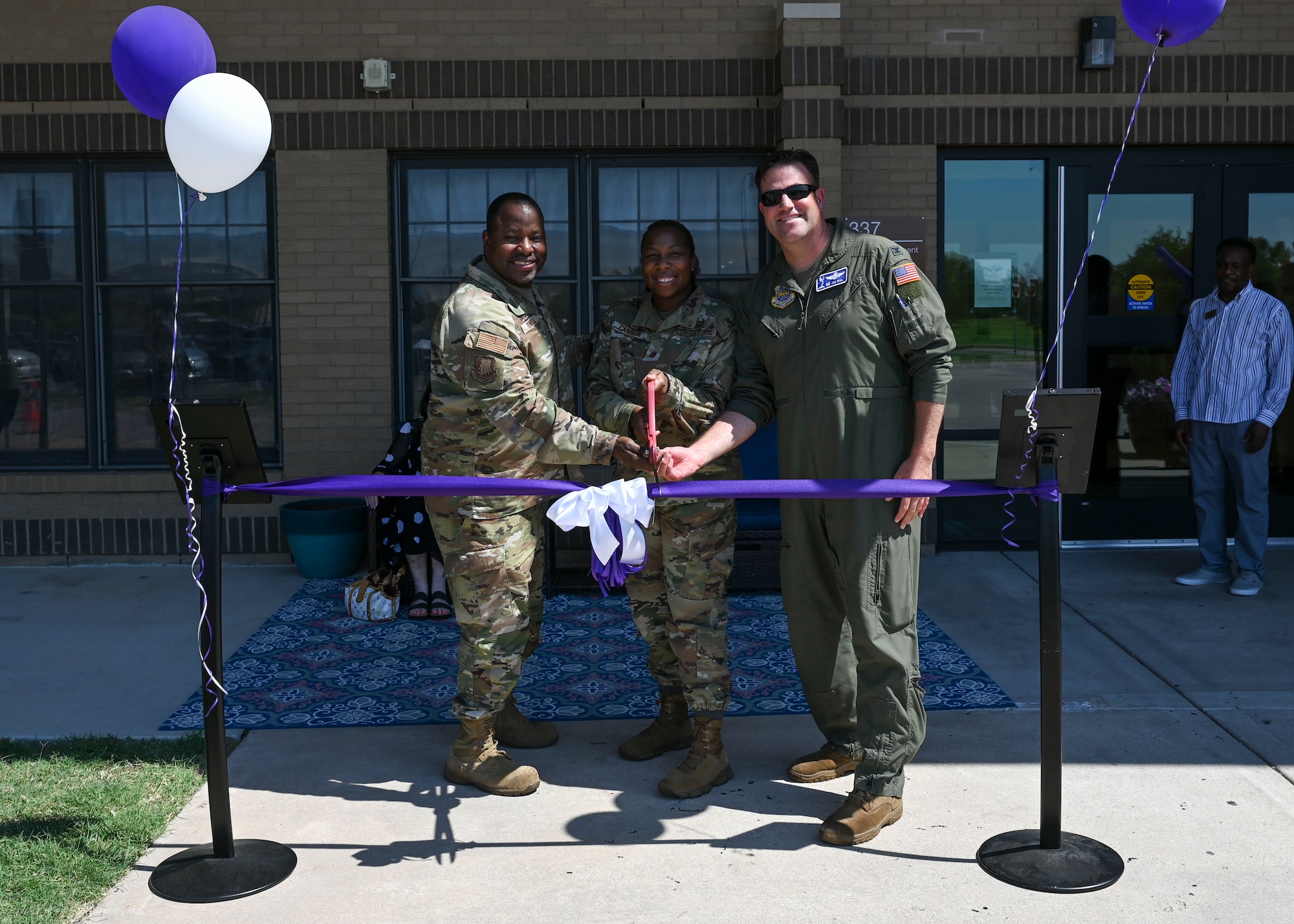 People in military uniforms use large scissors to cut a ribbon.
