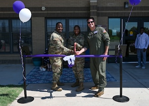 People in military uniforms use large scissors to cut a ribbon.