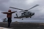 Aviation Electronics Technician Airman Apprentice David Benito, from Los Angeles, signals an MH-60R Sea Hawk helicopter, attached to Helicopter Maritime Strike Squadron (HSM) 71, as it takes off from the flight deck of the Nimitz-class aircraft carrier USS Abraham Lincoln (CVN 72).