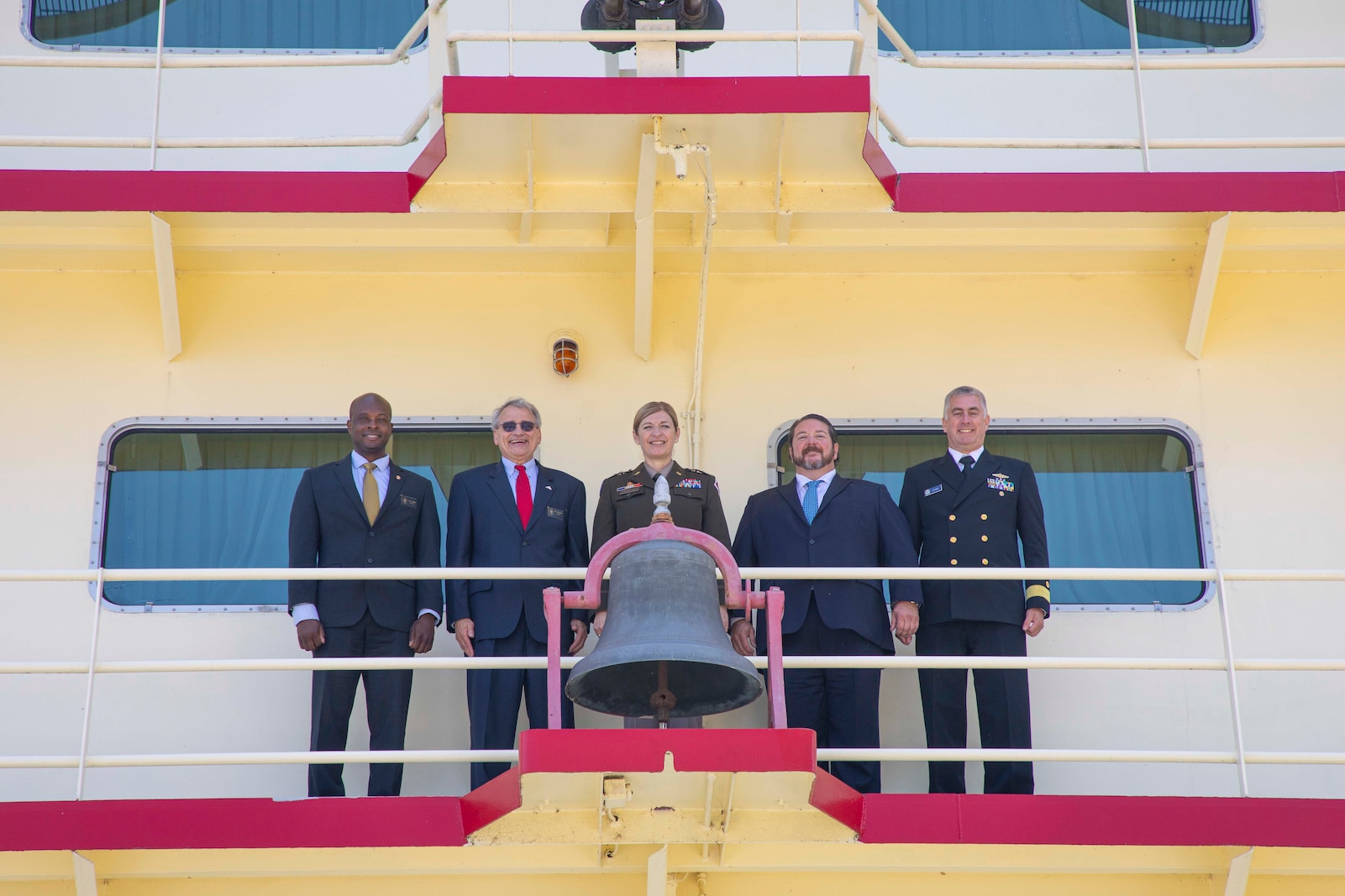 People posed behind a bell on a boat