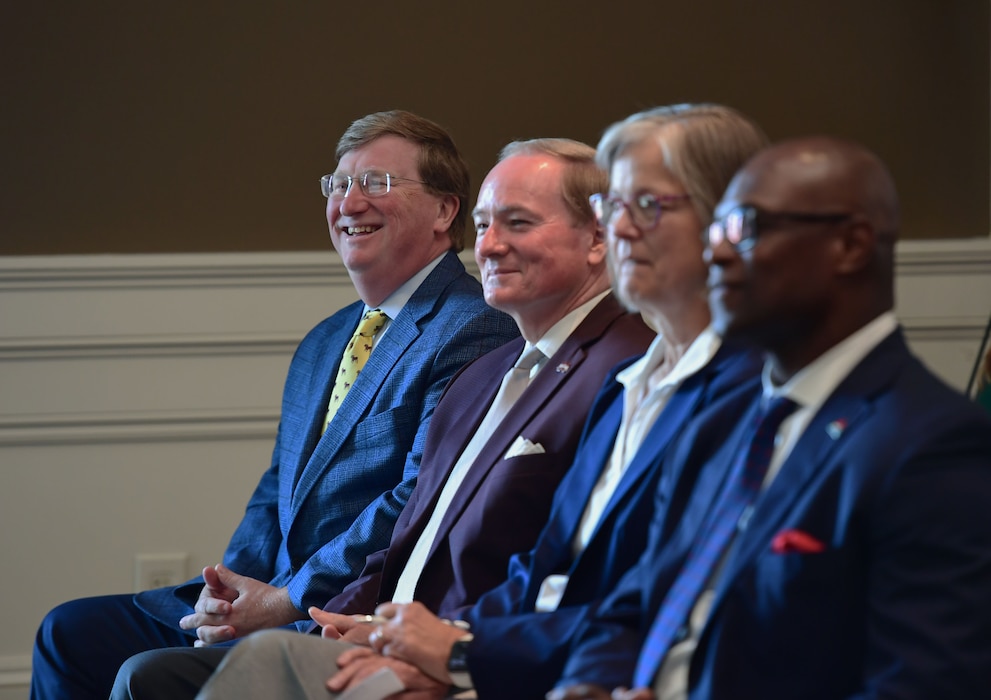 A group of people sit in chairs while smiling.