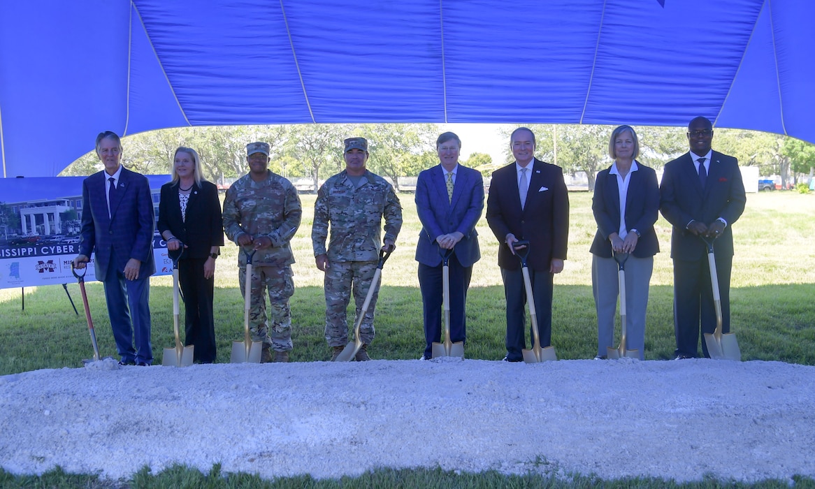 A group of people hold shovels while standing behind a mound of dirt.