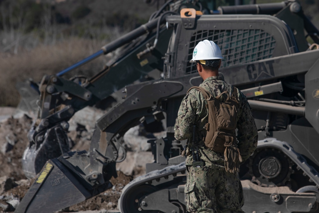 A U.S. Navy Sailor with Airfield Construction Company Bravo, Naval Mobile Construction Battalion 5, Naval Construction Force, ground guides a compact track loader during Operation Resilient Spear at Vandenberg Space Force Base, California, Aug. 10, 2025. Operation Resilient Spear is an opportunity for Marines with Marine Wing Support Squadron 372, Marine Air Control Group 38, 3rd Marine Aircraft Wing, to integrate and train with NMCB-5, through Base Recovery After Attack and Airfield Damage Repair Training to increase interoperability between Marine Corps engineers and Navy Seabees. (U.S. Marine Corps photo by Lance Cpl. Alexander Vaughn)