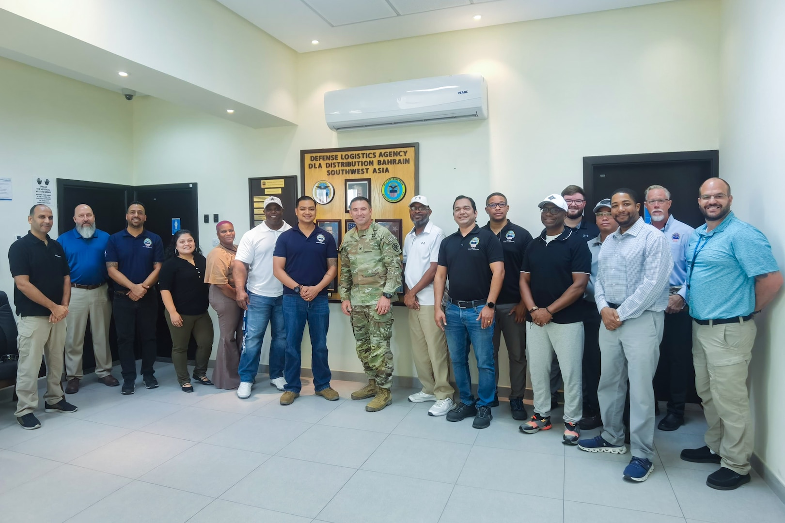 A group of people, with a man wearing a camouflage military uniform standing in the center, pose for a group photo.