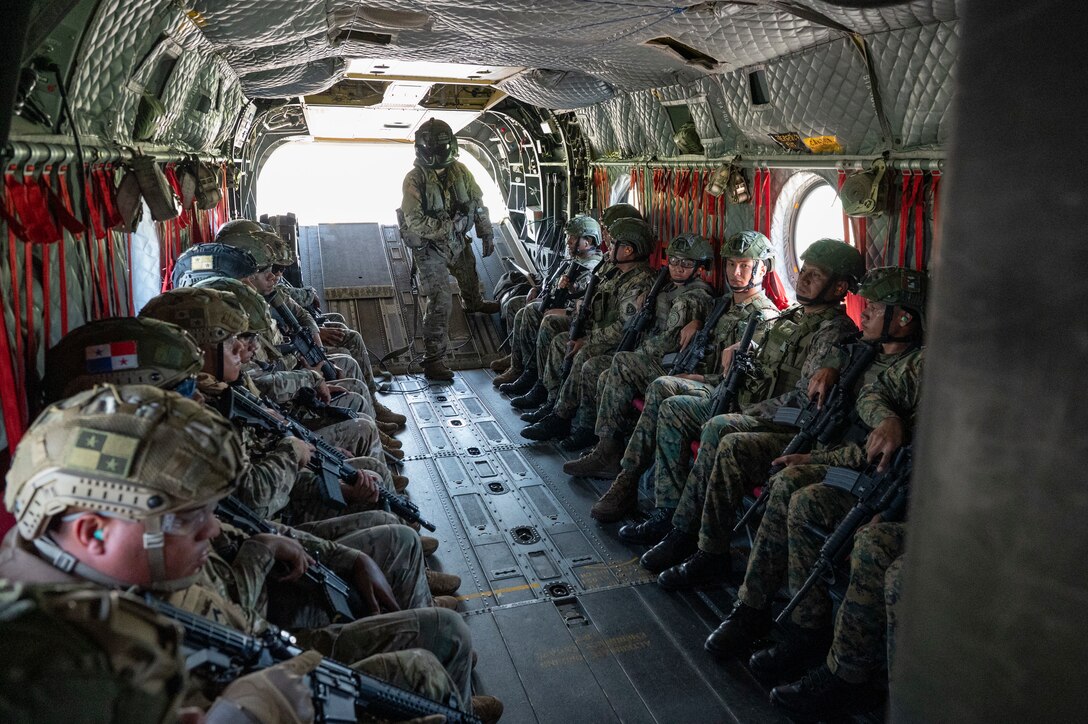 Panamanian soldiers sit in a CH-47 Chinook during as U.S. Army Sgt. James Coppola, 1st Battalion, 228th Aviation Regiment aircrewman, communicates to the pilots, prior to liftoff during PANAMAX-Alpha Phase I at Panama Pacifico International Airport, Panama, July 14, 2025. PANAMAX is an annual joint exercise designed to enhance interoperability among participating nations and strengthen their ability to conduct multinational operations, particularly to defend the Panama Canal. (U.S. Air Force photo by Staff Sgt. Sadie Colbert)