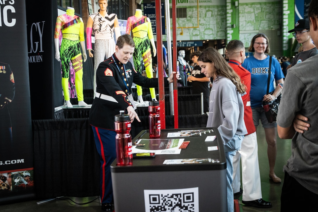 U.S. Marine Corps Staff Sgt. Lucy Warmbrodt, a Musician Technical Assistant with 9th Marine Corps District, speaks about the Musician Enlistment Option Program during the Drum Corps International World Championship in Indianapolis, August 9, 2025. The ensemble, known as “The Commandant’s Own,” showcased their musical precision, discipline and professionalism, captivating an audience of thousands gathered to witness top drum corps from around the world. (U.S. Marine Corps photo by Sgt. Devin Horton)