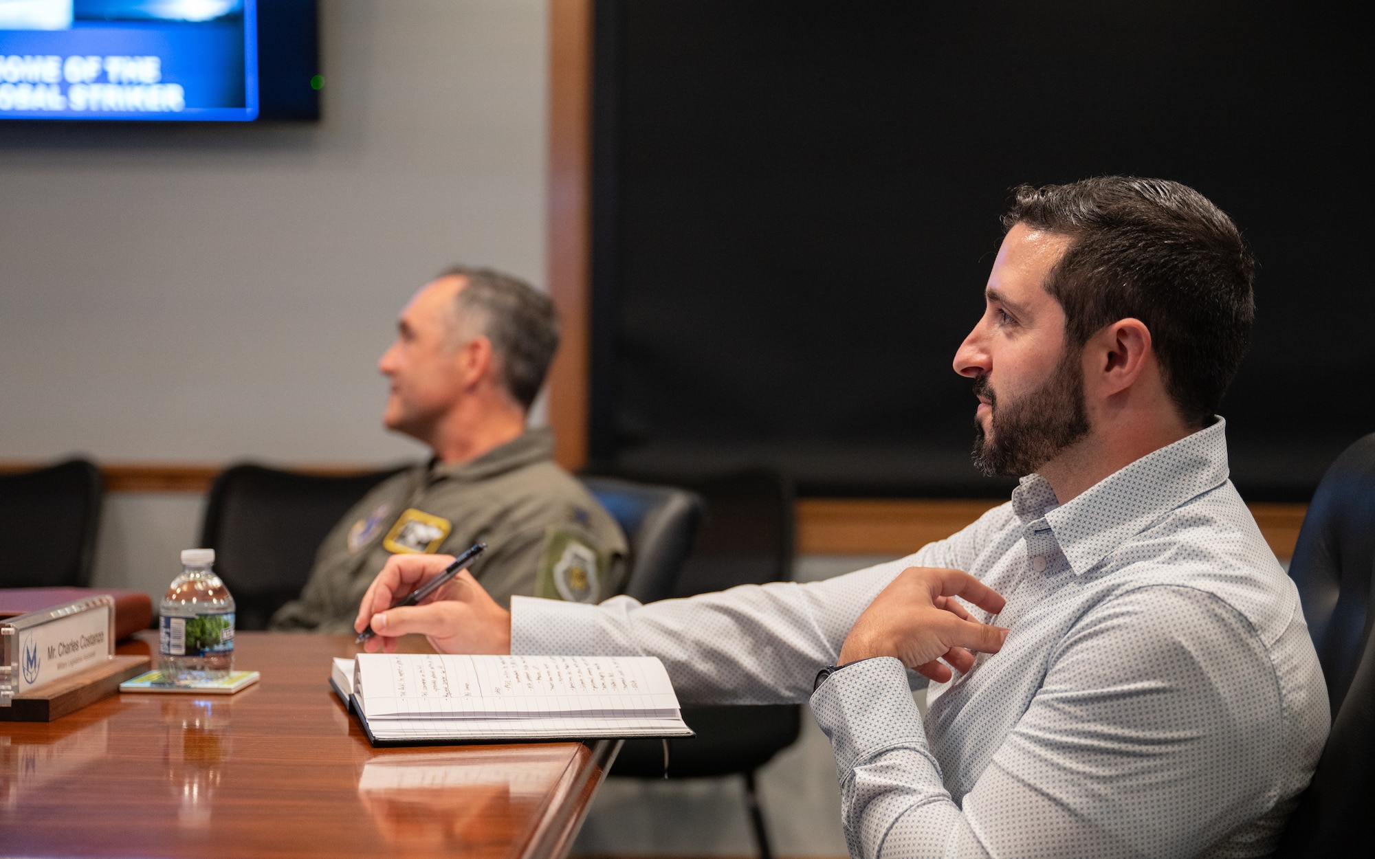 Charles Costanzo sits at a conference table, receiving a briefing during a staff delegation.