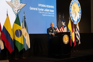 A man in a blue military uniform speaks at a podium flanked on each side by various nation flags.