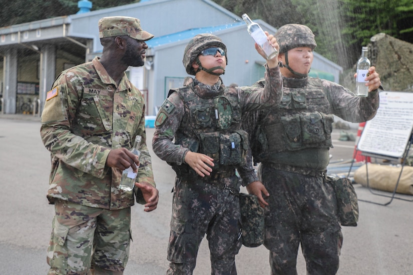 A U.S. soldier and two South Korean troops each hold a water bottle outdoors.