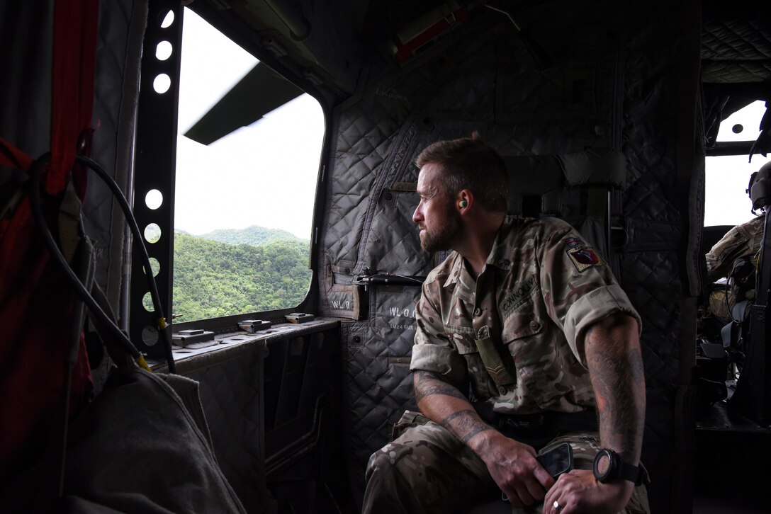 A British Army Training Support Unit Belize (BATSUB) member looks out of a CH-47 Chinook, during exercise AGILE BEAR 25, in Belize, Aug. 5, 2025. Subject matter expert exchanges with partner forces focused on specialized skills such as small Unmanned Aircraft Systems (sUAS) operations, combatives, Tactical Combat Casualty Care (TCCC), Helocast procedures, and conducting troop movements to remote locations. (U.S. Air Force photo by Tech. Sgt. Dylan Rossitto)