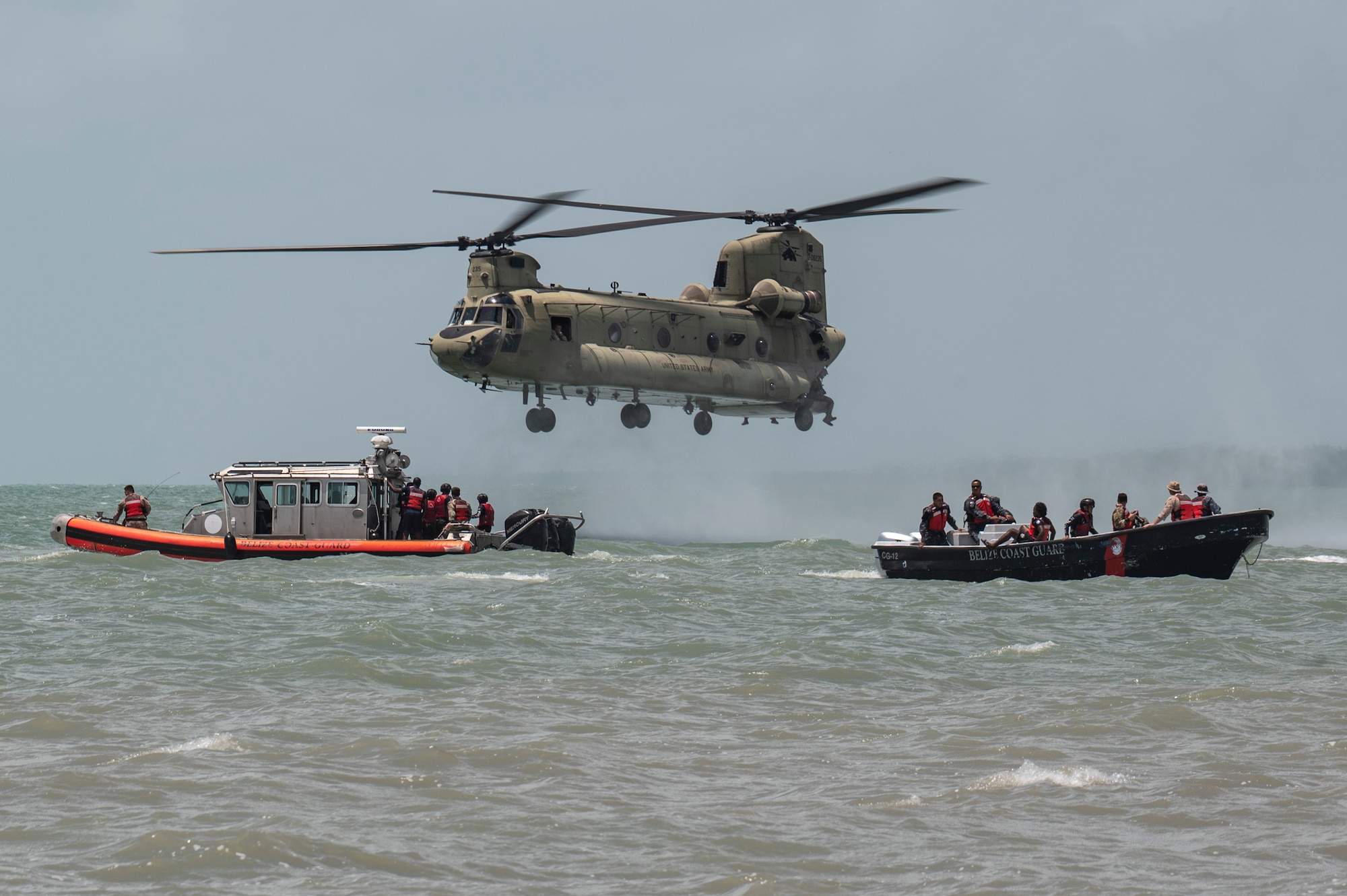 A CH-47 Chinook assigned to 1st Battalion, 228th Aviation Regiment out of Soto Cano Air Base, Honduras, hovers near Belize Defence Force and Belize Coast Guard safety boats for helocast practice during AGILE BEAR 25, Belize City, Belize, Aug. 6, 2025. The exercise aims to strengthen the readiness of U.S. and partner nation forces to respond effectively during a disaster and in countering transnational criminal organizations through various events. Key participants included Joint Task Force-Bravo, Belize Coast Guard, Belize Defence Force, U.S. Embassy-Belize, and the British Army Training Support Unit-Belize (BATSUB).  (U.S. Air Force photo by Staff Sgt. Sadie Colbert)