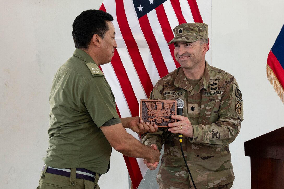 Belize Defence Force Brig. Gen. Azariel Loria, BDF commander, receives a plaque and shakes hands with U.S. Army Lt. Col. Wayne Hancock, Joint Task Force-Bravo J3 plans, logistics and operations adjutant general, at the conclusion of AGILE BEAR 25, Belize City, Belize, Aug. 6, 2025. Training with defense forces focuses on specialized skills such as subject matter expert exchanges for small Unmanned Aircraft Systems (sUAS) operations, combatives, Tactical Combat Casualty Care (TCCC), helocast procedures, and conducting troop movements to remote locations. (U.S. Air Force photo by Staff Sgt. Sadie Colbert)