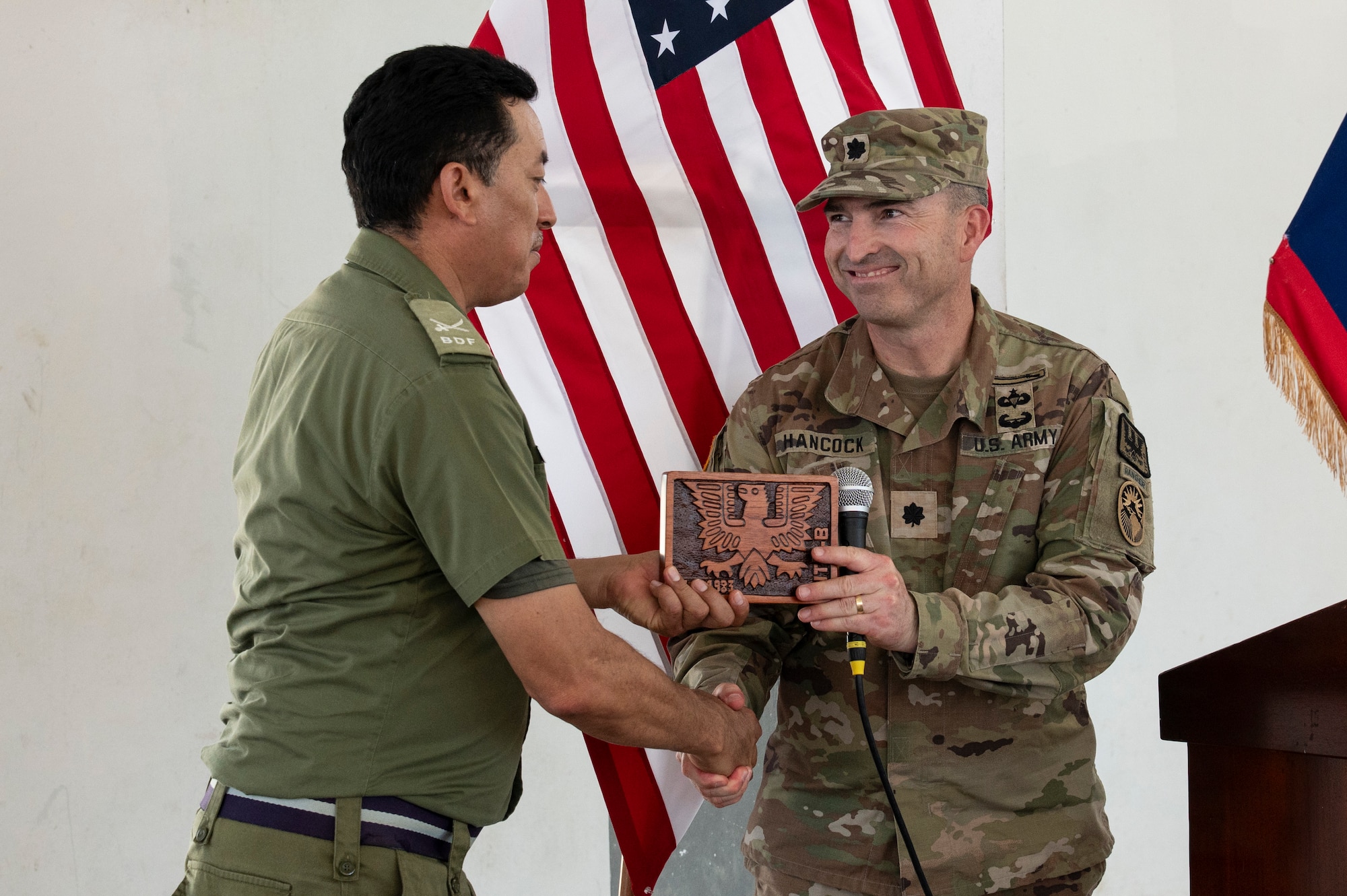 Belize Defence Force Brig. Gen. Azariel Loria, BDF commander, receives a plaque and shakes hands with U.S. Army Lt. Col. Wayne Hancock, Joint Task Force-Bravo J3 plans, logistics and operations adjutant general, at the conclusion of AGILE BEAR 25, Belize City, Belize, Aug. 6, 2025. Training with defense forces focuses on specialized skills such as subject matter expert exchanges for small Unmanned Aircraft Systems (sUAS) operations, combatives, Tactical Combat Casualty Care (TCCC), helocast procedures, and conducting troop movements to remote locations. (U.S. Air Force photo by Staff Sgt. Sadie Colbert)