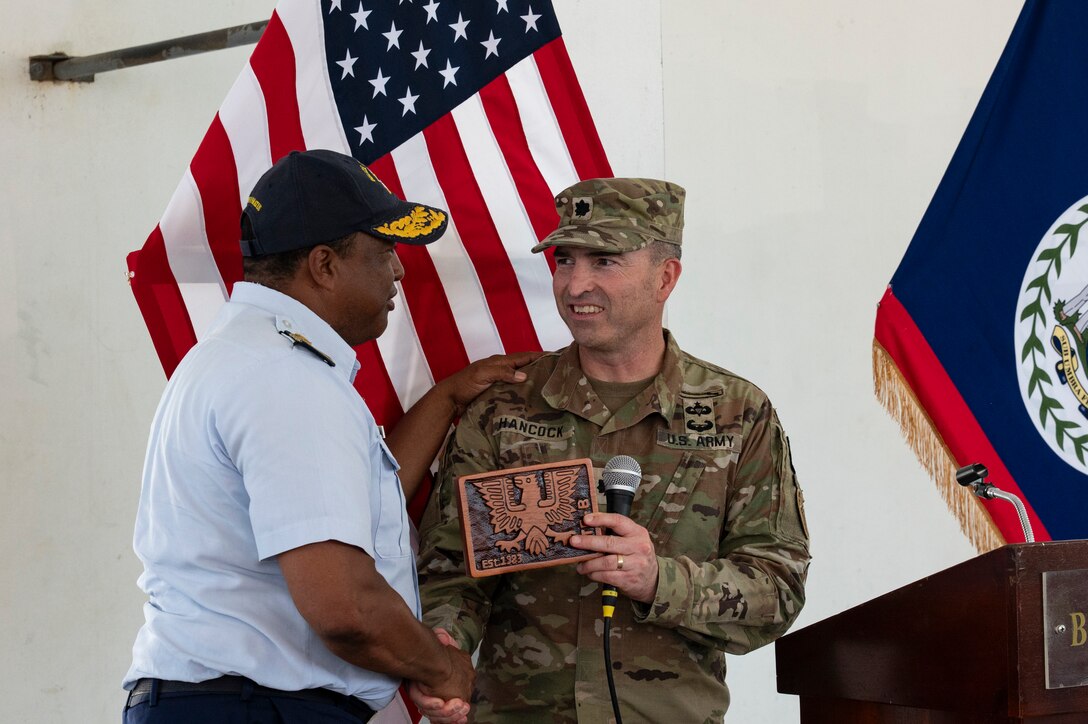 Belize Coast Guard Capt. Gregory Soberanis, BCG vice commandant, receives a plaque and shakes hands with U.S. Army Lt. Col. Wayne Hancock, Joint Task Force-Bravo J3 plans, logistics and operations adjutant general, at the conclusion of AGILE BEAR 25, Belize City, Belize, Aug. 6, 2025. Training with defense forces focuses on specialized skills such as subject matter expert exchanges for small Unmanned Aircraft Systems (sUAS) operations, combatives, Tactical Combat Casualty Care (TCCC), helocast procedures, and conducting troop movements to remote locations. (U.S. Air Force photo by Staff Sgt. Sadie Colbert)