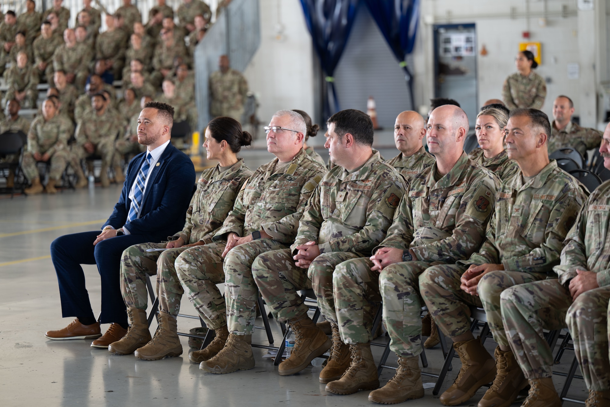 Airmen, senior leaders and civilian officials sit in chairs and bleachers