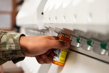 An Airman fills a pill bottle with medication.