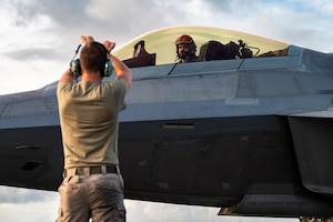 A U.S. Air Force F-22 Raptor is marshalled by Senior Airman Dylan Gurski, a crew chief, both deployed with the 3rd Air Expeditionary Wing, during exercise Resolute Force Pacific 2025 in Tinian, North Mariana Islands, July 17, 2025.