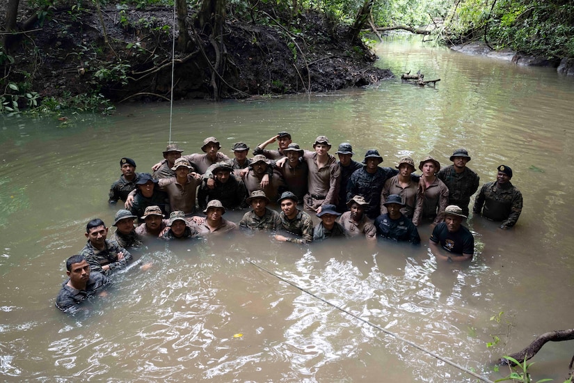 A group of service members poses for a photo in a river in a jungle.