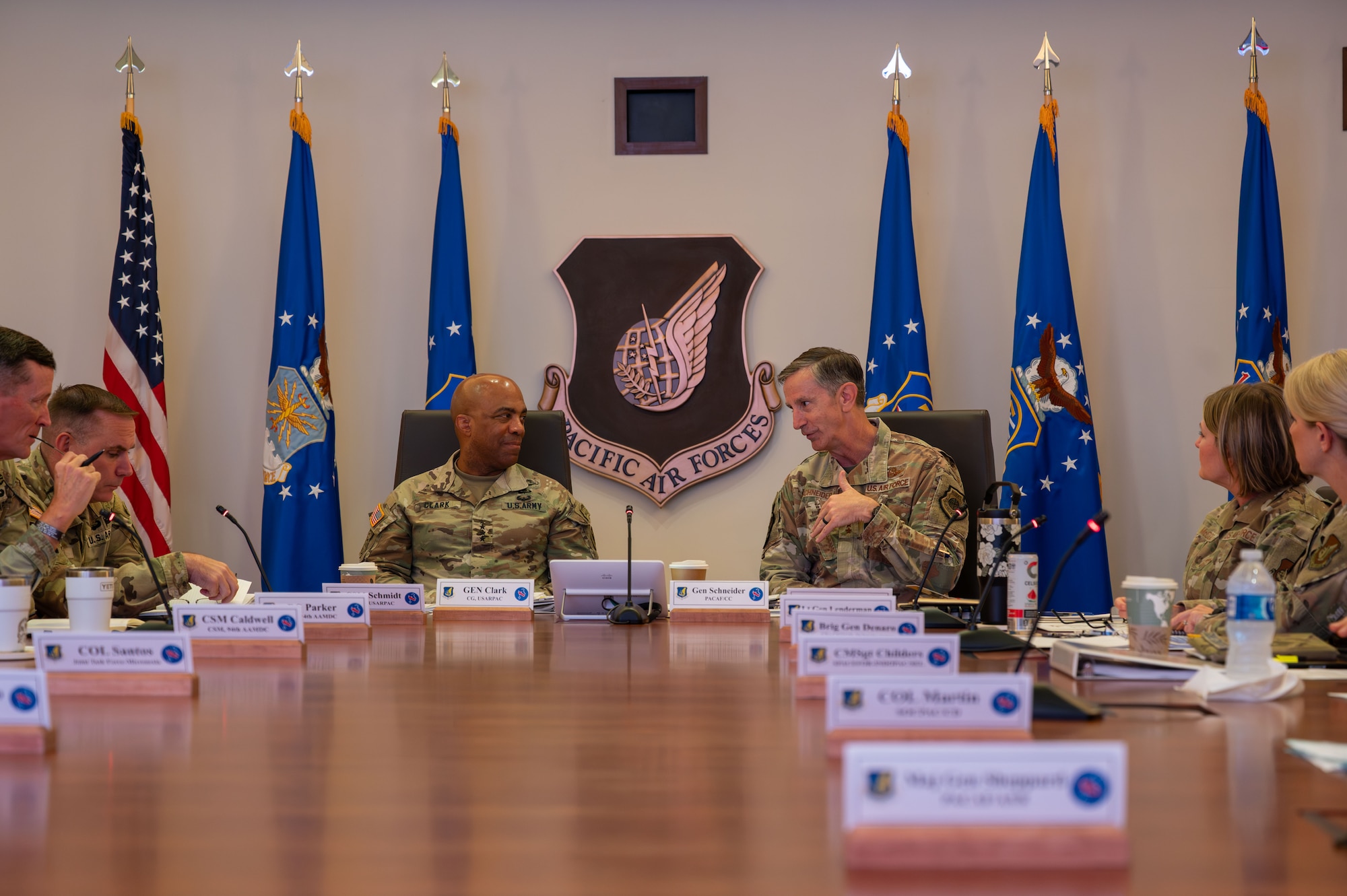 U.S. Air Force Gen. Kevin Schneider, Pacific Air Forces commander, and U.S. Army Gen. Ronald Clark, U.S. Army Pacific commander, hosted the next iteration of the Cross-Component Integration Forum to discuss strategies and best practices for fostering greater interoperability and integration among the U.S. Army and Air Force units in the Indo-Pacific at Joint Base Pearl Harbor-Hickam, Hawaii, Aug. 19, 2025. This collaboration is essential for cohesive joint operations, especially in implementing Agile Combat Employment (ACE) and Multi-Domain Operations (MDO). (U.S. Air Force photo by Staff Sgt. Elizabeth Taranto)

The two leaders are seated at a large table alongside other leaders in their commands.