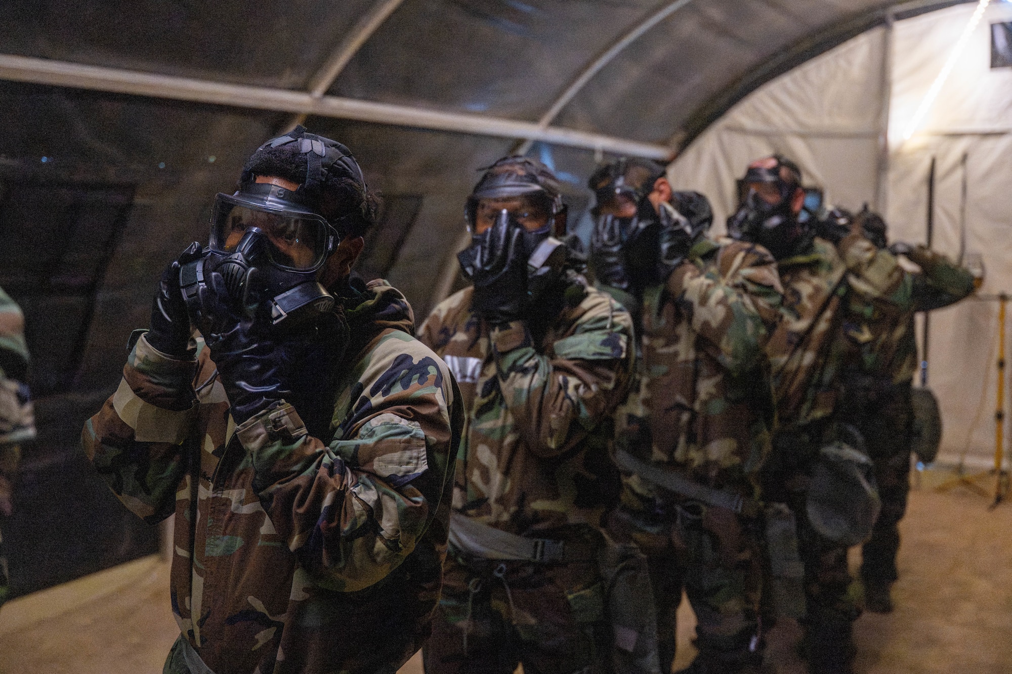 Four Airman place their hand on the center of the gas mask to remove it while inside a gas chamber for training.