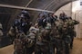 Four Airman place their hand on the center of the gas mask to remove it while inside a gas chamber for training.