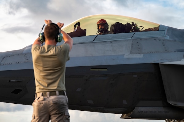 A U.S. Air Force F-22 Raptor is marshalled by Senior Airman Dylan Gurski, a crew chief, both deployed with the 3rd Air Expeditionary Wing, during exercise Resolute Force Pacific 2025 in Tinian, North Mariana Islands, July 17, 2025.