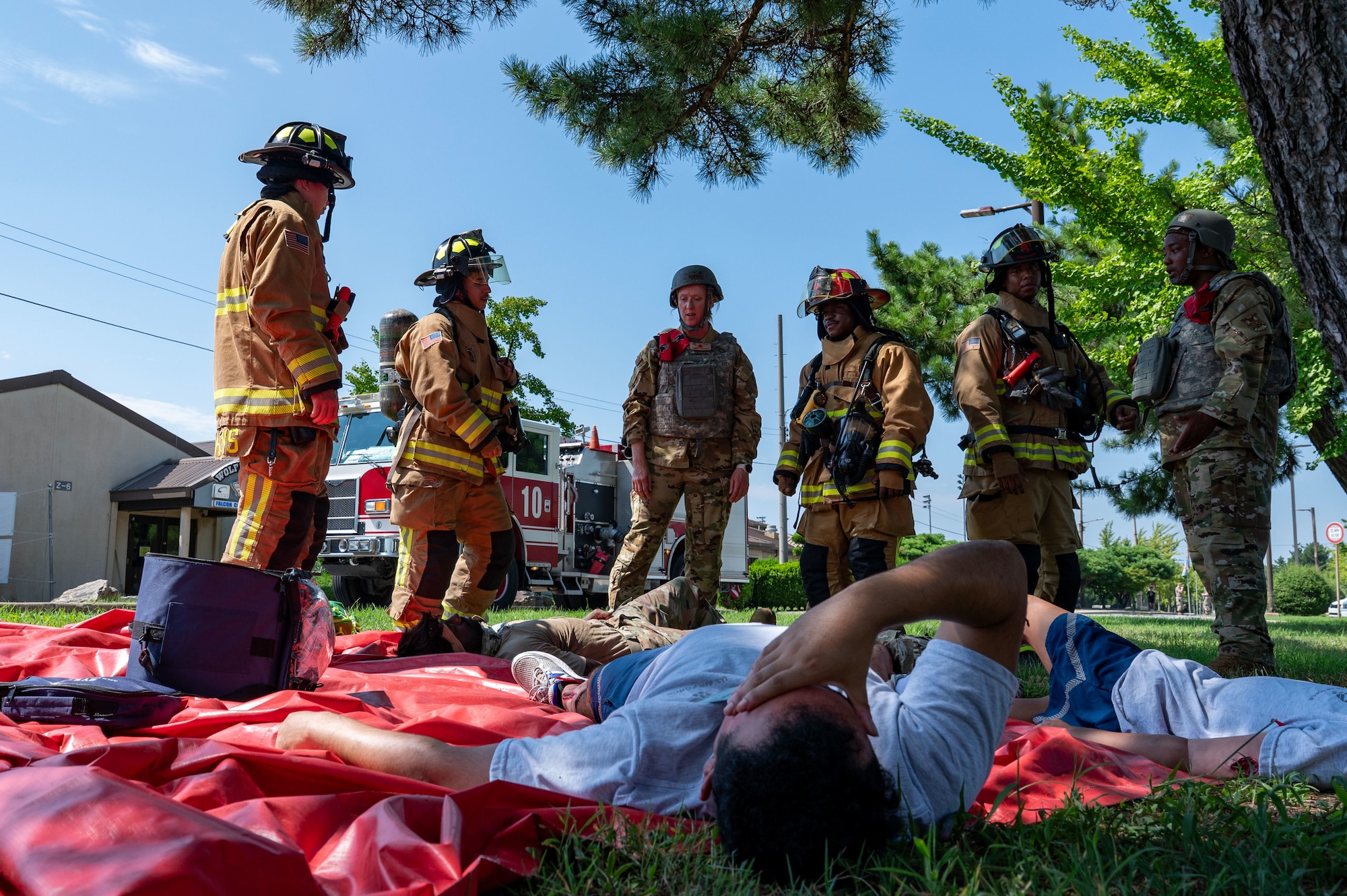 A man is on the ground acting like he's in pain while firefighters stand around him