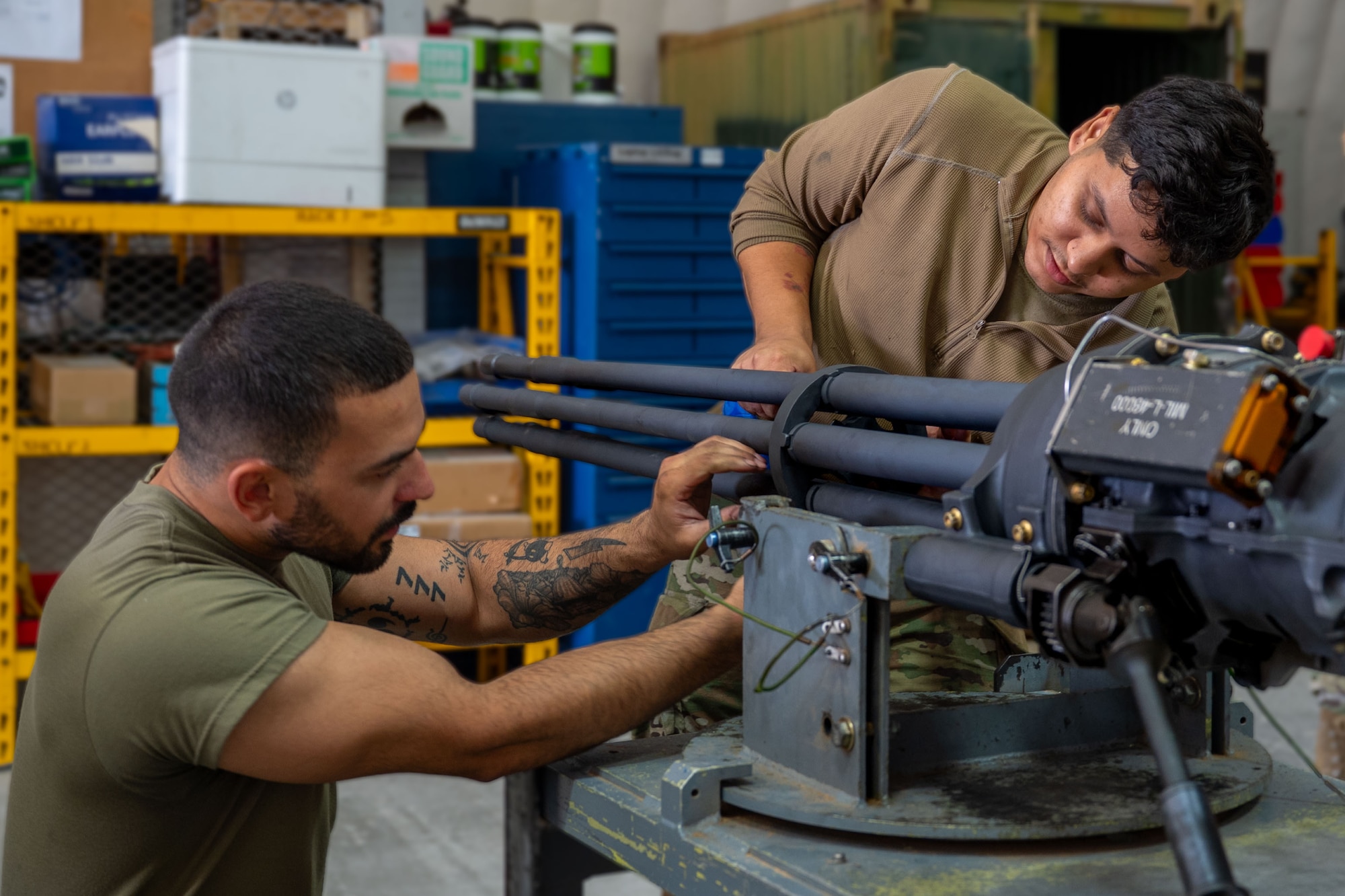 Two Airmen attach a mid-barrel clamp to a M61A1 Gatling gun.