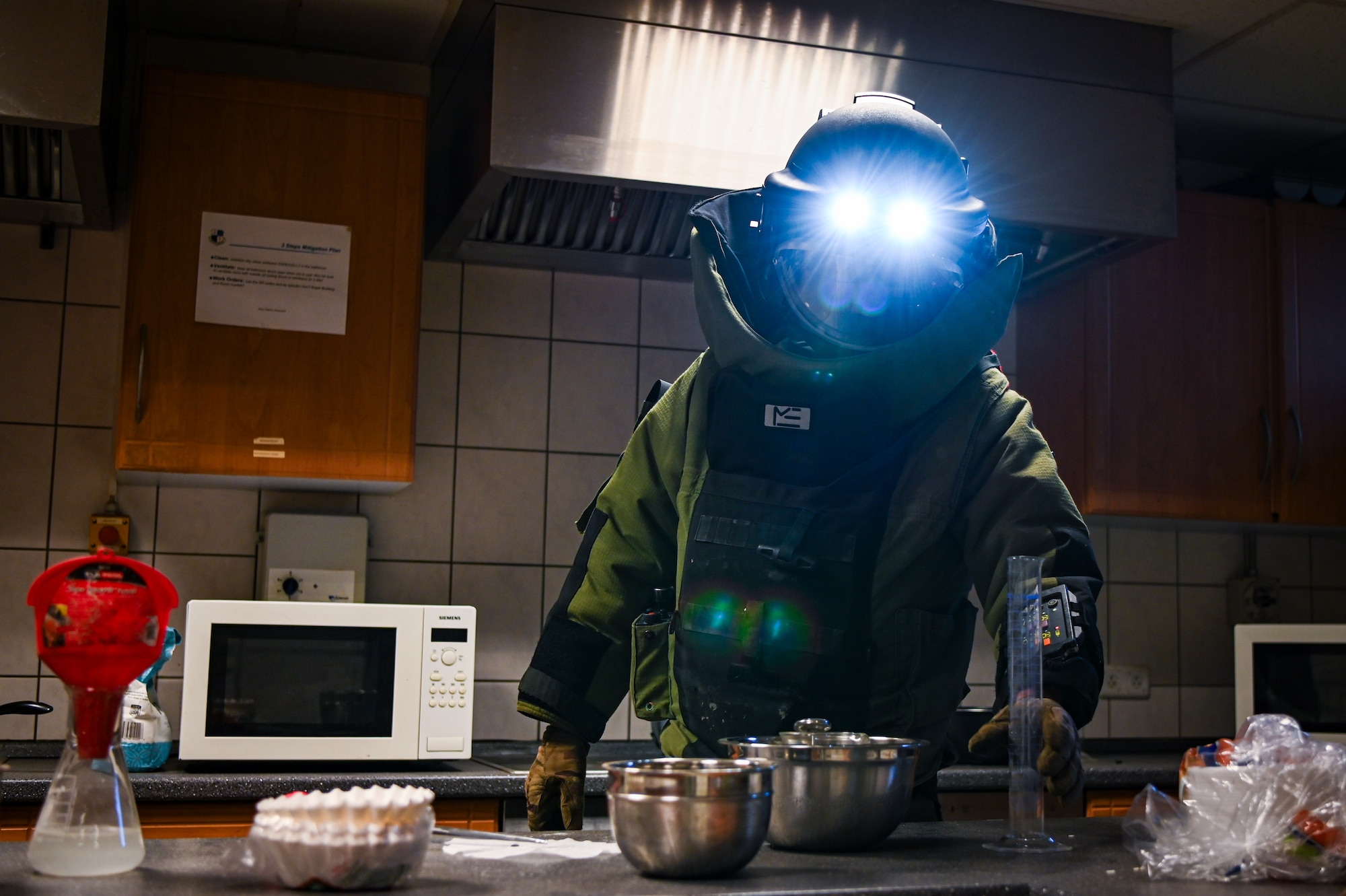 A person in a bomb suit handles measuring equipment in an IED lab.