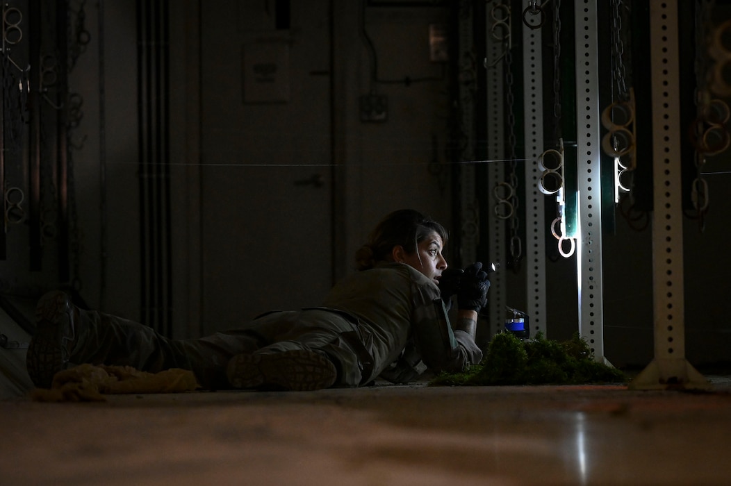 A person holding a flashlight crawls along the ground in a dark room.