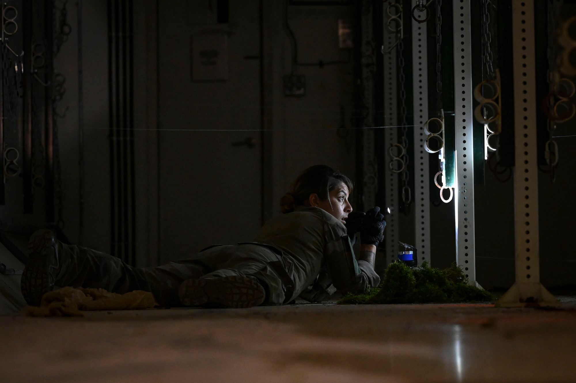 A person holding a flashlight crawls along the ground in a dark room.