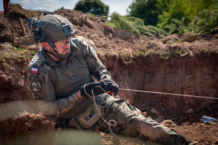 A person wearing protective equipment in a trench pulls on a rope.
