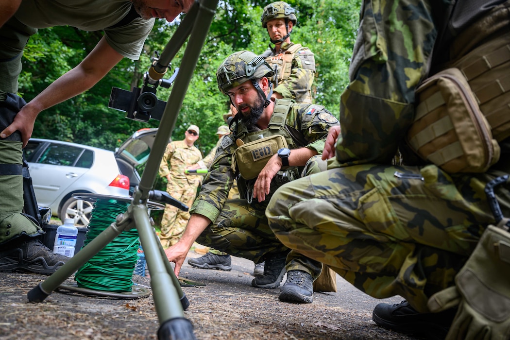 A group of people wearing protective gear gather around EOD equipment.