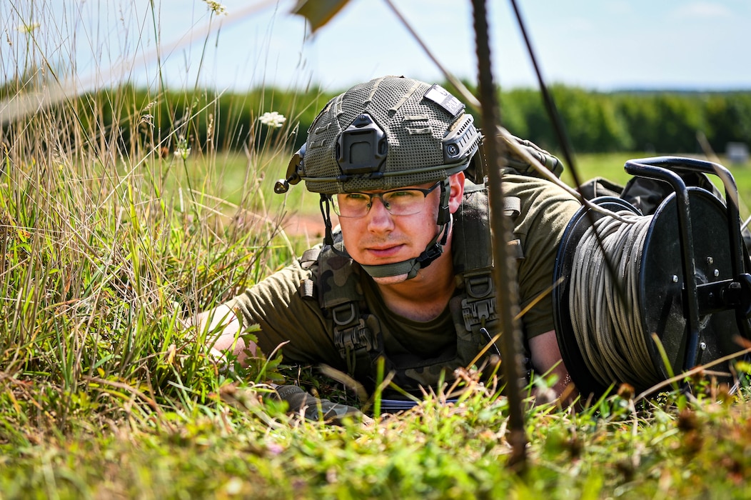 A person with a helmet crawls through long grass.
