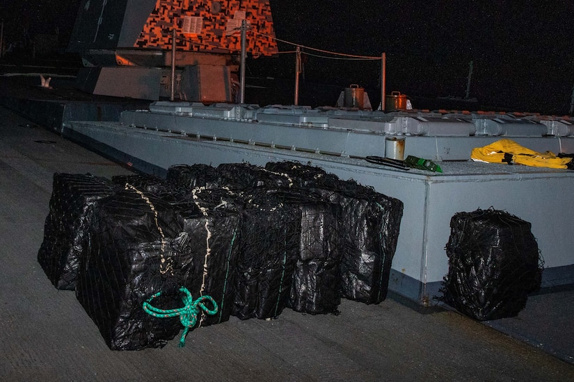 Large bales wrapped in black plastic are stacked together on a ship.