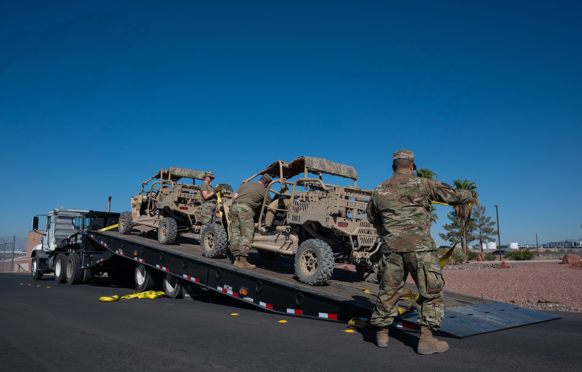 Two Airmen, one on a trailer alongside two utility vehicles, and one standing on the ground nearby.