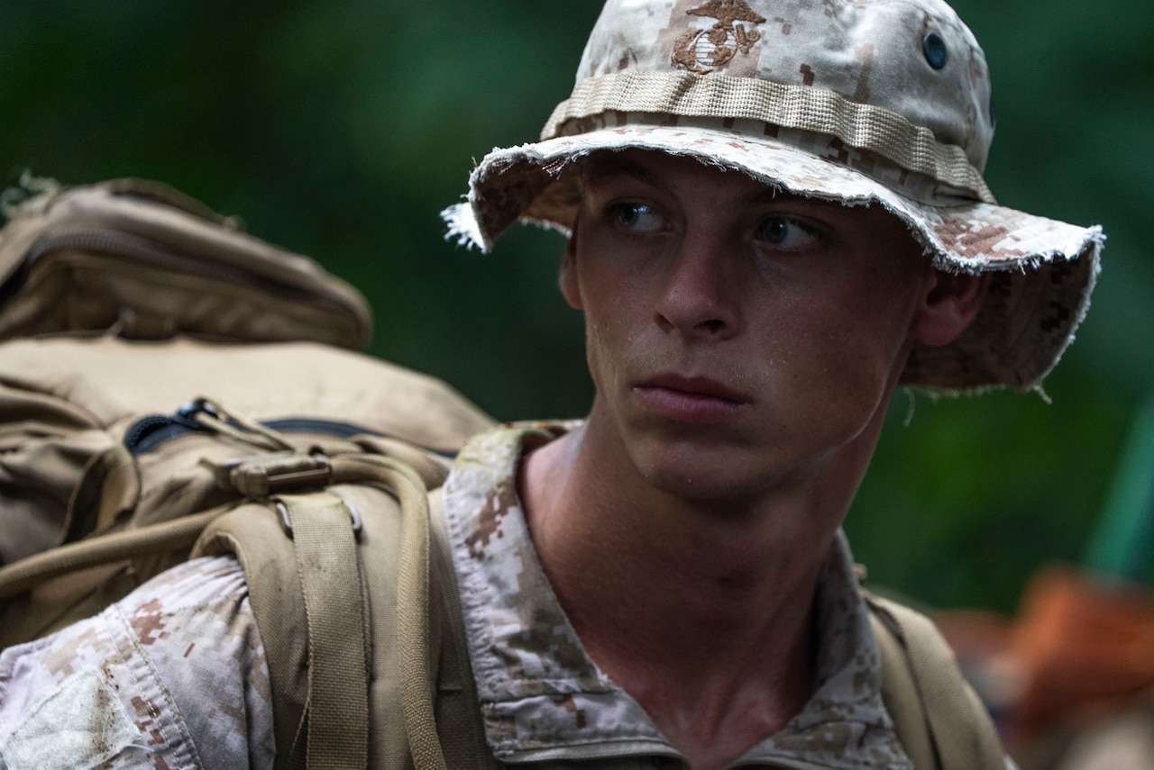 A Marine wearing a hat looks off camera while in the jungle.